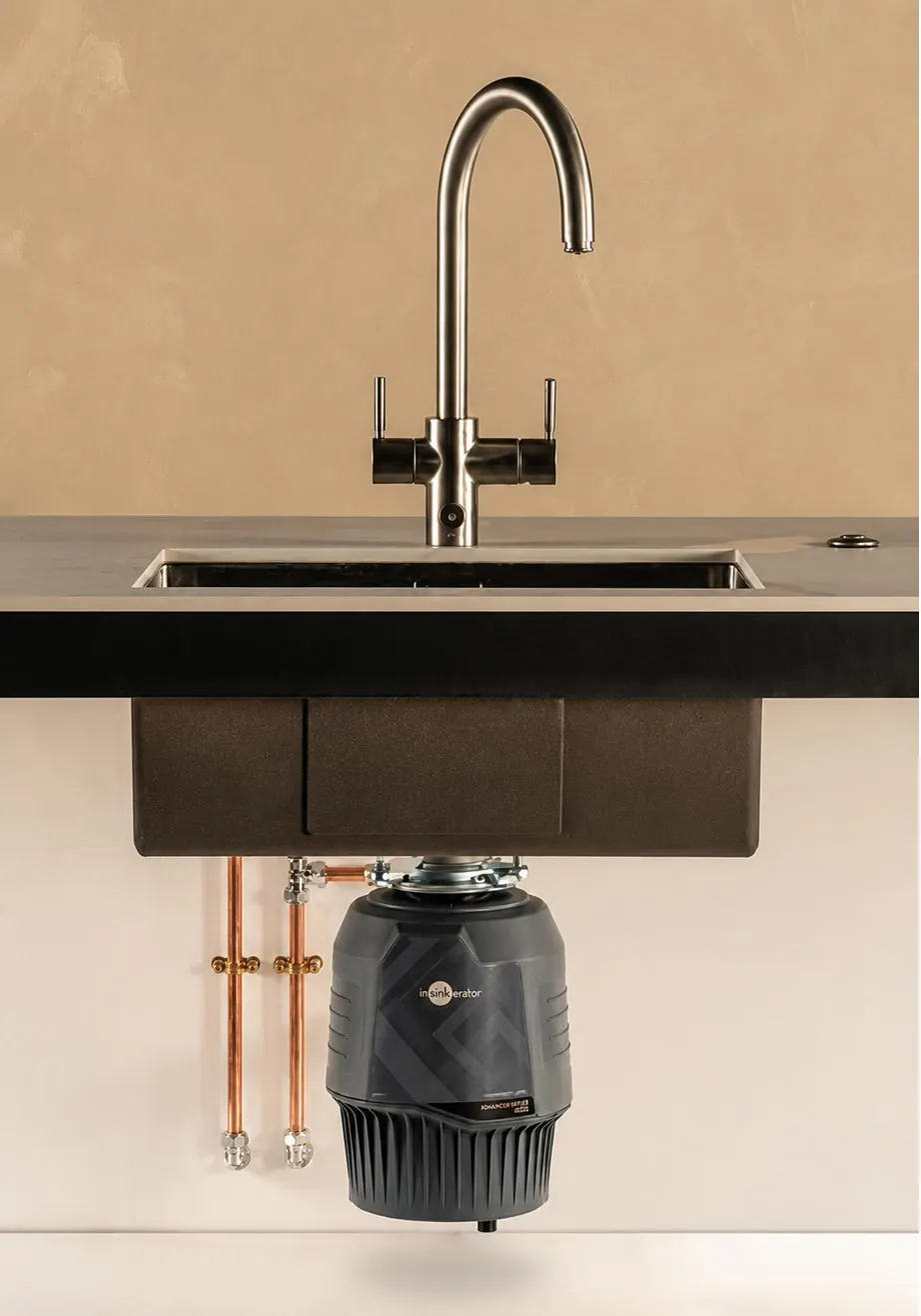 A food waste disposer installed under the sink, connected to the waste pipe inside the kitchen cabinet.
